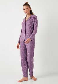 Violetit pyjamat, joissa on valkoisia pilkkuja, sisältäen napitettavan paidan, jossa on kaulus ja pitkät hihat, yhdistettynä yhteensopiviin pitkään housuun.