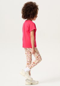 T-shirt rose vif à manches courtes associé à un legging léger crème avec un motif de fruits colorés. Des baskets blanches et des chaussettes de cheville complètent le look.