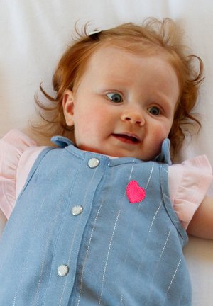 Bébé portant une salopette en denim rayée bleu clair, ornée d'un cœur rose brodé, accompagnée d'un t-shirt rose doux en dessous.