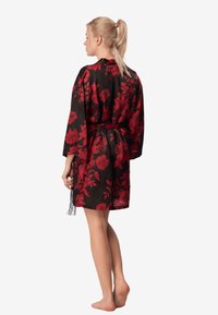 Czarny kimono z czerwonym kwiecistym nadrukiem, długimi rękawami, wiązaniem w talii oraz frędzlami na dole, charakteryzujące się lekką, gładką teksturą.