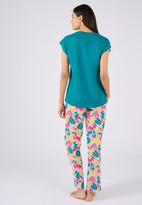 Top turchese a maniche corte abbinato a pantaloni colorati e stampati con disegni floreali e fogliari in rosa, giallo e verde su uno sfondo bianco.