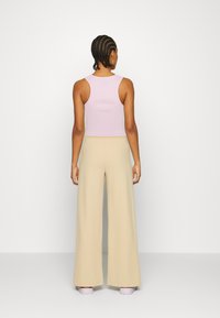 Top cropped em lilás com textura canelada, combinado com calças largas em bege; apresenta um design simples e textura suave, visto de costas.