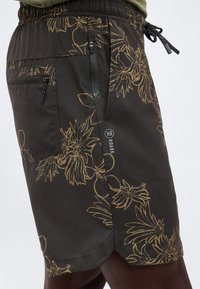 Σκούρα σορτς με μπεζ λουλουδάτο σχέδιο, δύο τσέπες με φερμουάρ, σούρα στη μέση και λογότυπο "Roark" στο πλάι.