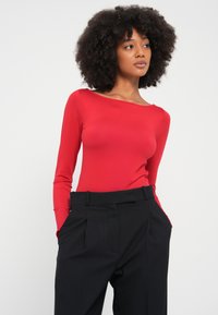 Piros, hosszú ujjú body széles nyakkivágással, magas derekú, fekete csíkos nadrággal párosítva. Selymes tapintású, testhez simuló fazon.