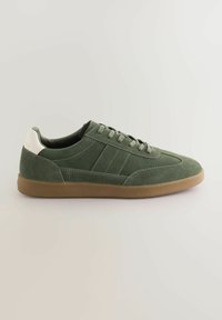 Sneaker en suede vert avec un profil bas, présentant un accent blanc au talon et une semelle en caoutchouc marron clair. Comprend des lacets ton sur ton et des détails cousus.
