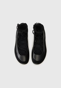 Des chaussures noires présentent un dessus lisse et brillant avec une surface texturée, un bout arrondi et un laçage croisé. Semelle en caoutchouc avec détail de grip.
