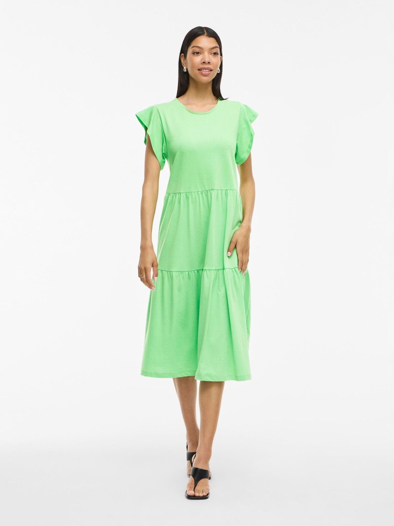 Zielona bawełniana sukienka z okrągłym dekoltem, krótkimi falbanowymi rękawami, warstwowym fasonem i luźnym krojem, w połączeniu z czarnymi sandałami.