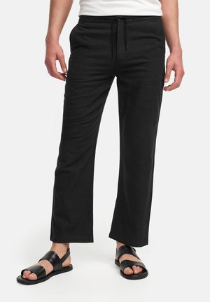 Svart, løstsittende bukser laget av lett stoff, med elastisk midje og snøring samt sidelommer. Kombinert med svarte sandaler.