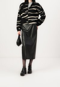 Kobieta ubrana w czarną i białą w paski kurtkę na zamek, czarną skórzaną spódnicę midi, czarne rajstopy, buty na platformie oraz trzymająca czarną torebkę.