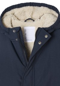 Marineblauer Mantel mit weicher, cremefarbener Fleece-Innenausstattung, durchgehendem Reißverschluss, Druckknöpfen und einer Kapuze mit Kordelzug. Innenpflegeetikett sichtbar.