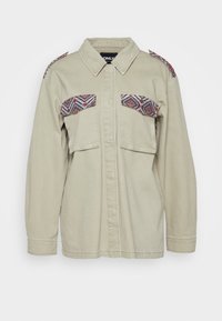 Light beige jacket with long sleeves, two chest pockets, and patterned accents on shoulders, featuring a collared neck and button front.