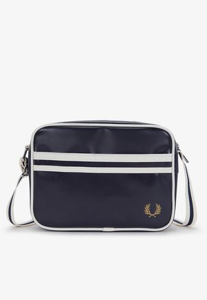 Bolso de hombro rectangular azul marino con ribete blanco, dos rayas blancas horizontales, correa ajustable y logo de corona de laurel dorada en el frente.