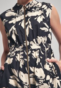 Floral-printed dress in navy and cream, featuring a collared neck, full zipper, and gathered waist. Sleeveless design with side pockets.