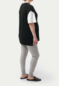 Svart stickad väst över en vit T-shirt, kombinerat med grå leggings och svarta slip-on skor. Slät textur, avslappnad passform och minimalistisk design.