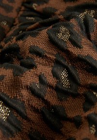 Tessuto tessuto marrone e nero caratterizzato da un motivo a stampa di leopardo in rilievo con accenti metallici, che mostra dettagli di tessitura intricati.
