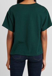 Mörkgrön bomull t-shirt med avslappnad passform, korta ärmar och rundad halsringning. Buren med mörka jeans i denim, vilket visar en enkel design.