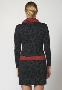 Schwarzes Kleid mit floralem Muster, langen Ärmeln und einem roten strukturierten Taillenbund. Das Design verfügt über komplexe Muster auf einem glatten Stoff.