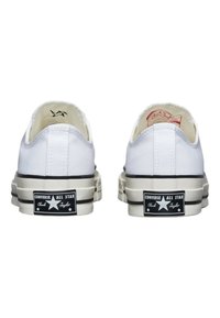 Vita kanvas sneakers med låg design, svarta gummisulor och svarta/vita logopatchar på hälarna. Har stickade sömmar.
