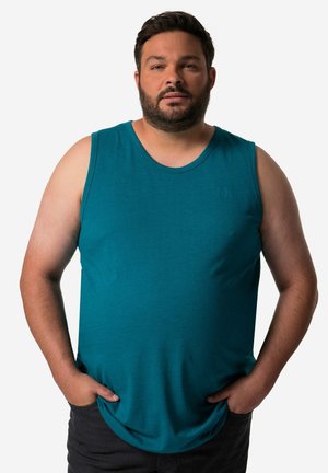 Tyrkysový bezrukávový bavlněný top s kulatým výstřihem a volným střihem. Výrazné logo reliéfně vytištěné na hrudi, v kombinaci s tmavými džíny.