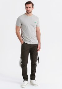 T-shirt a maniche corte grigio chiaro con un piccolo etichetta verde, abbinato a pantaloni cargo verde scuro con tasche e orli con cordino. Sneakers bianche.