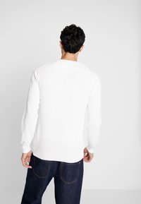 Weißer strukturierter Pullover mit langen Ärmeln und Rundhalsausschnitt, kombiniert mit dunkelblauen Jeans. Einfaches Design, keine Muster oder Akzente sichtbar.