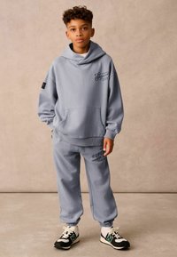 Lysblå hoodie med en forlommem og logo broderi; matchende joggers med ribbede manchetter og trykte mærkedetaljer; sorte sneakers.