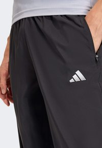 Schwarze Sporthose aus glattem, leichtem Stoff mit elastischem Bund. Verfügt über eine Reißverschlusstasche und ein weißes Logo als Akzent.