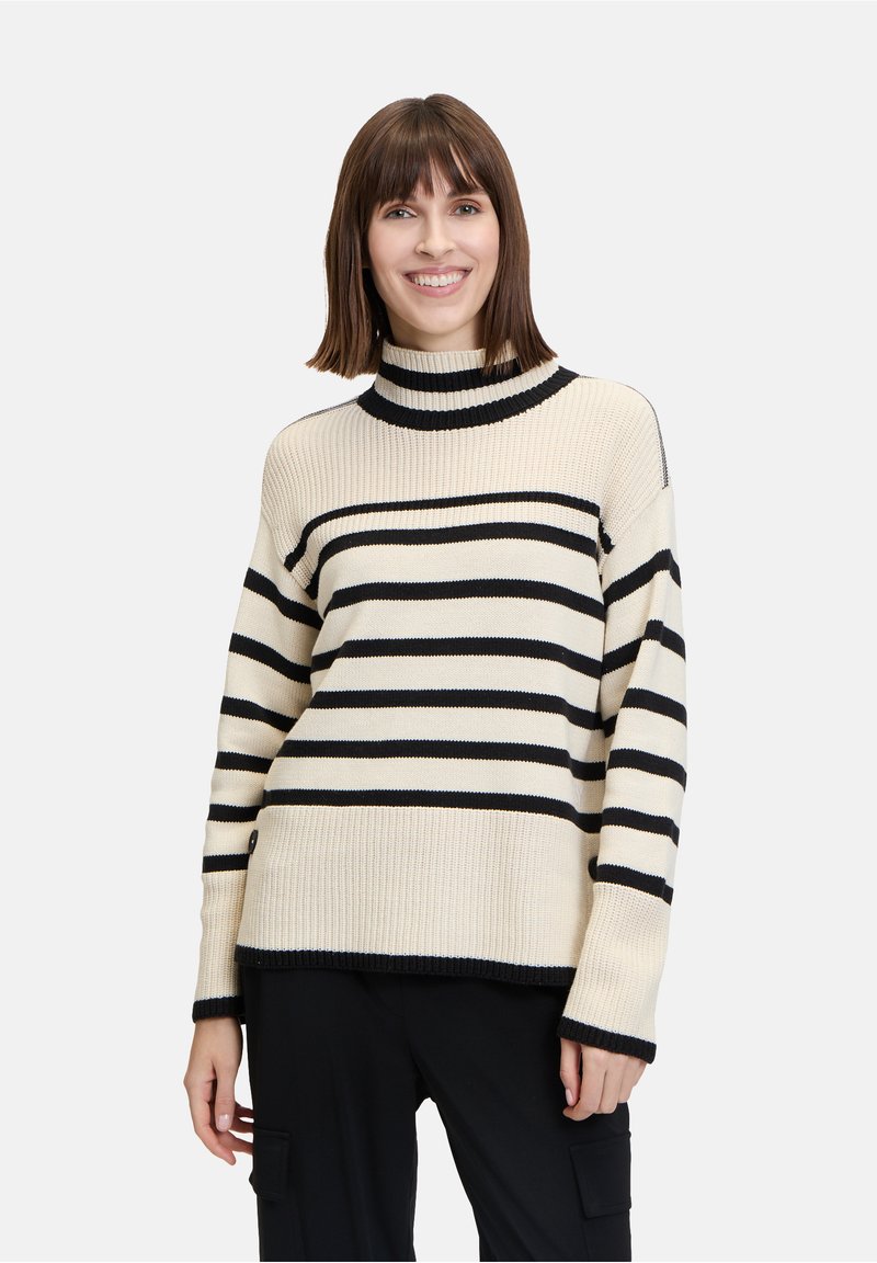 Cremfarbener Rollkragenpullover mit schwarzen horizontalen Streifen, gerippter Textur, langen Ärmeln und lässiger Passform, kombiniert mit dunklen Hosen.