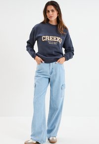 Marineblauwe sweatshirt met "Creeks Original Since 1974" in lichtbeige. Gecombineerd met lichtblauwe wijdere cargobroek met zijzakken.