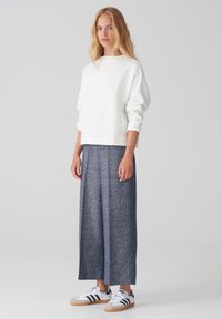 White oversized sweatshirt, textured navy wide-leg trousers, and white sneakers with navy stripes. Simple design and relaxed fit.