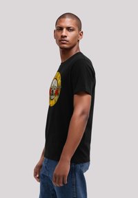 Zwarte T-shirt met een ronde grafische afbeelding van een schedel, rozen en gele accenten. Relaxte pasvorm, gebreide stof, korte mouwen, klassieke halslijn.