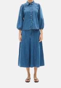 Conjunto de denim que incluye una camisa de botones con mangas abullonadas y una falda de pierna ancha a juego, ambos en un tono azul medio y de textura suave.