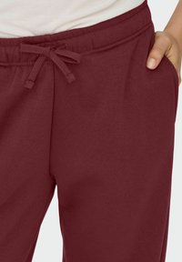 Bordeaux farvede sweatpants med snøre i taljen, sidelommer, blødt stof og afslappet pasform. Materialet ser glat og let ud.