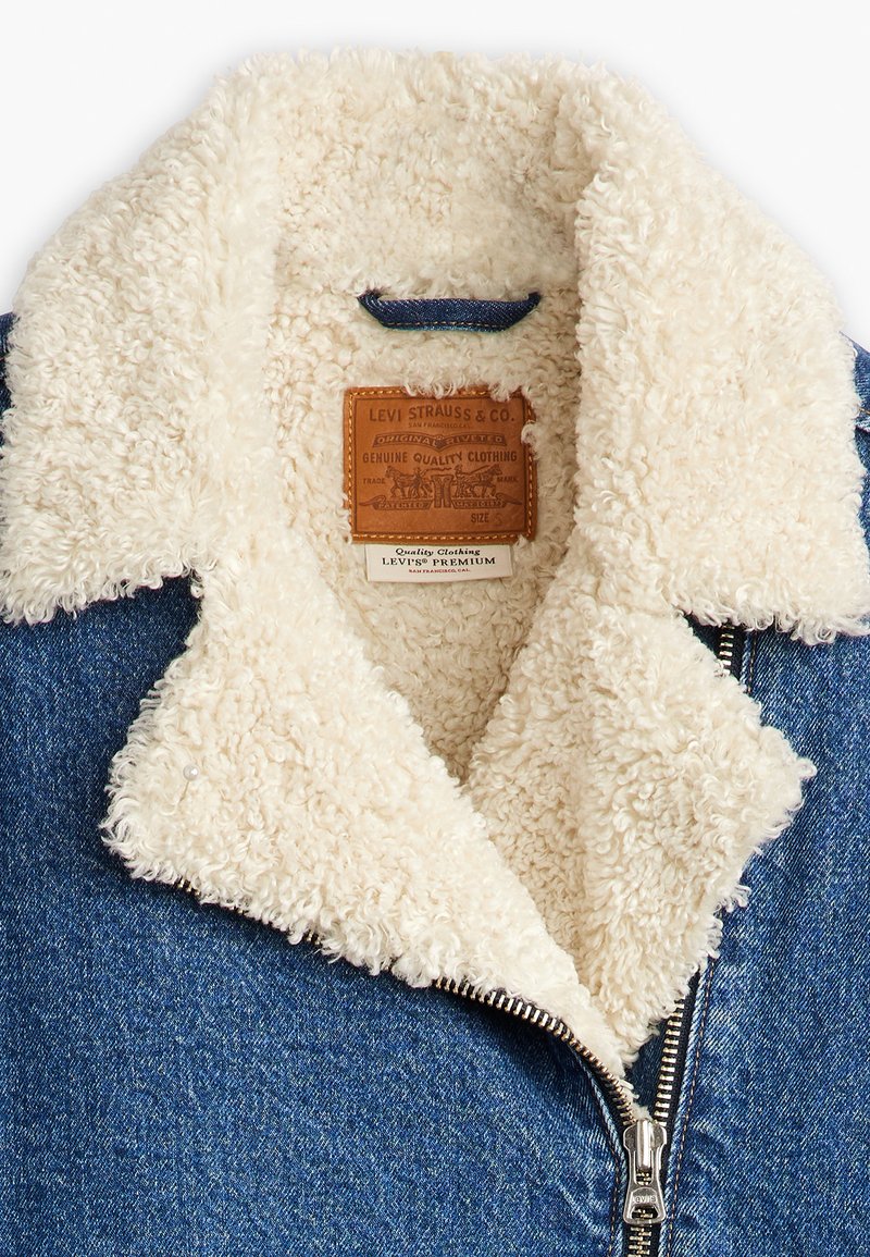 Veste en jean avec un col en fausse fourrure crème, fermeture éclair et une étiquette en cuir avec les détails de la marque. Intérieur doublé de doux polaire.