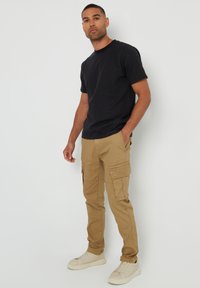 Schwarzes Baumwoll-T-Shirt, kombiniert mit hellbraunen Cargo-Hosen mit Seitentaschen und lässigem Schnitt. Getragen mit weißen Sneakers.