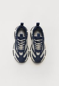 Adidași donker albastri și gri, cu panouri din plasă, accente albe, soles groase și detalii reflectorizante. Prezintă șireturi plate și o bucată de prindere.