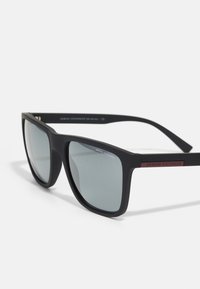 Ochelari de soare negri cu finisaj mat, formă rectangulară, lentile gri și un accent roșu cu inscripția "ARMANI EXCHANGE" pe braț.