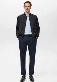 Giacca bomber nera con due tasche frontali, camicia dress azzurra chiara, pantaloni scuri su misura e scarpe nere lucide. Design semplice e moderno.