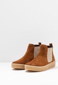 Stivaletti in suede marrone con pannelli laterali elastici beige e suola in gomma testurizzata, caratterizzati da un leggero tacco e linguette per una facile calzata.