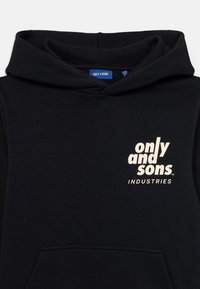 Felpa nera con tasca frontale, caratterizzata da un logo color crema con la scritta "only & sons" e "INDUSTRIES." Il materiale sembra morbido e strutturato.