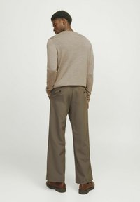 Maglione beige lavorato a maglia con maniche lunghe, abbinato a pantaloni larghi marroni con due tasche posteriori, indossato con calzature marroni.