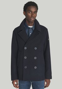 Cappotto in lana navy con design doppiopetto, ampie rever a punta e due tasche frontali. Presenta bottoni grigi e una finitura testurizzata.