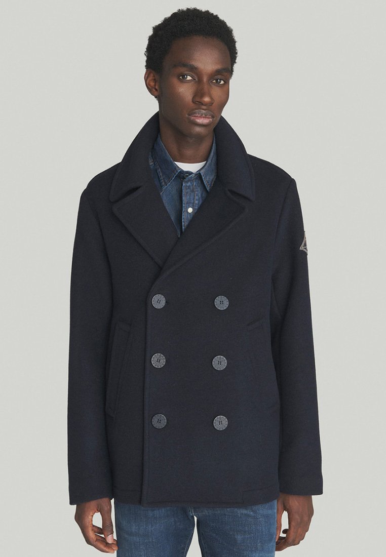 Cappotto in lana navy con design doppiopetto, ampie rever a punta e due tasche frontali. Presenta bottoni grigi e una finitura testurizzata.