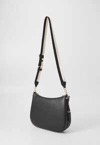 Black leather shoulder bag with a curved shape, adjustable black and cream strap, gold hardware accents, and smooth textured surface.