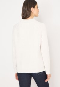 Pull en tricot couleur crème avec une texture côtelée, des manches raglan et un col arrondi, présentant une coupe légèrement ample et des poignets élastiques.