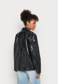 Casaco em vinil preto e brilhante, com um corte relaxado, gola com recortes e mangas longas. Design nas costas reto, com detalhes de costura discretos.
