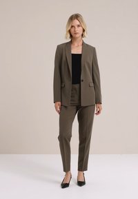 Olivově zelený tailored oblek s jedním knoflíkem na blejzru a slim-fit kalhotami, doplněný černým topem a černými lodičkami s špičatou špičkou.