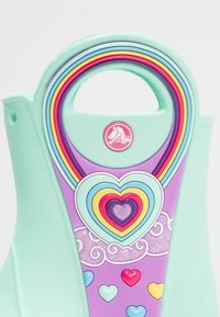 Produit vert menthe avec un design en forme de cœur, featuring des cœurs concentriques colorés et de petits accents en forme de cœur. Texture lisse et couleurs vibrantes.