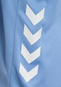 Quatre flèches chevrons blanches vers le bas imprimées sur un tissu bleu clair avec des coutures visibles le long de la couture latérale.