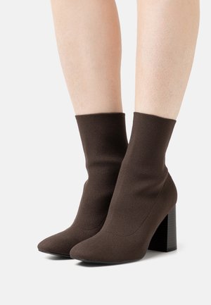Botas de ankle de punto marrones con punta afilada y un tacón bloque texturizado. La parte superior tiene un acabado suave, ofreciendo un ajuste ceñido alrededor del tobillo.